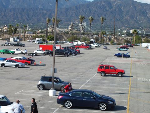 2003 Ford Crown Victoria - Elevated view of a busy event lot with a red Jeep, dark blue sedan, blue Mini and assorted cars below mountains.