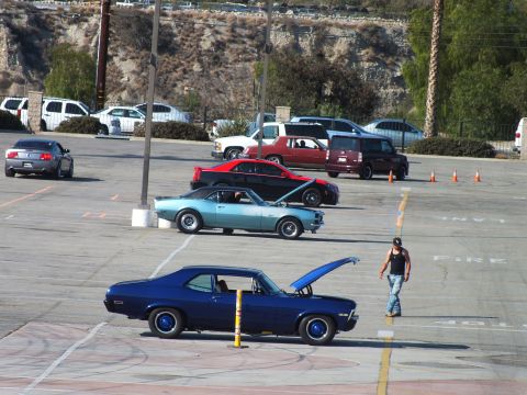2003 Ford Crown Victoria - blue classic coupe with raised hood and a turquoise Camaro sit staged in an event lot as a man walks past.