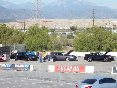 2003 Ford Crown Victoria - Black sedans, a wagon and a Mustang stage with hoods up behind MAVTV and Lucas Oil banners, mountains behind.