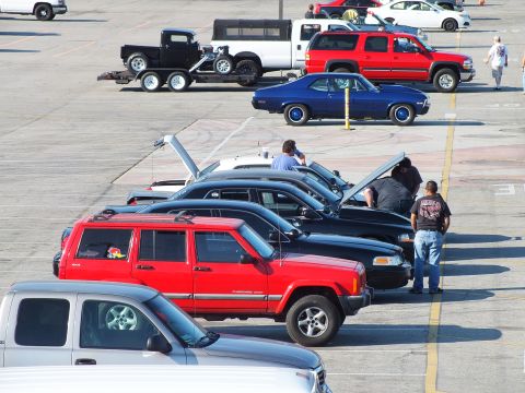 2003 Ford Crown Victoria - People inspect a row of cars with raised hoods including a red Jeep and blue coupe, a trailered hot rod beyond.