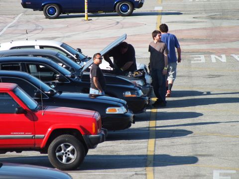 2003 Ford Crown Victoria - Men stand around an open hood among a row of parked SUVs in a paved lot, with a red Jeep Cherokee nearest the camera.