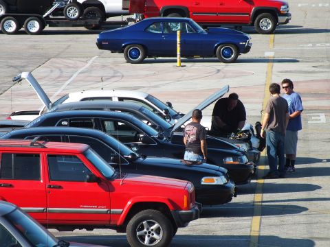 2003 Ford Crown Victoria - row of parked SUVs with raised hoods sits in a lot while a blue classic coupe is parked in the background.