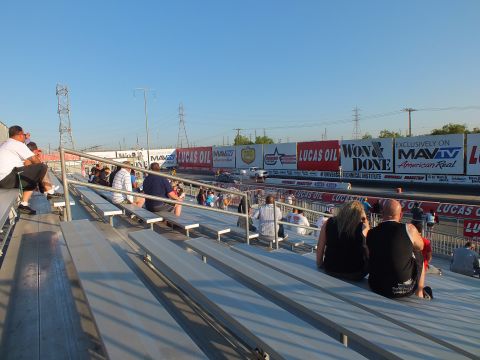 2003 Ford Crown Victoria - Spectators sit on aluminum grandstand bleachers overlooking a drag strip lined with Lucas Oil and MAVTV banners.