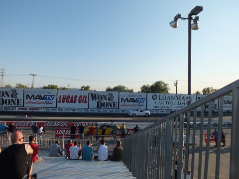 2003 Ford Crown Victoria - Spectators sit along a drag strip at dusk as a white car runs the lane past Lucas Oil and Won and Done banners.