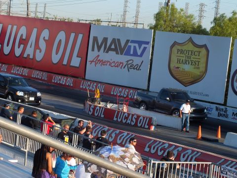 2003 Ford Crown Victoria - dark pickup runs the drag strip lane past Lucas Oil, MAVTV and Protect the Harvest banners while crew stand at the wall.