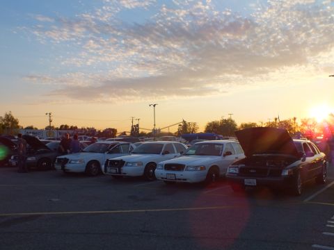 2003 Ford Crown Victoria - lineup of white full-size sedans with raised hoods sits in a parking lot as the sun sets behind them.