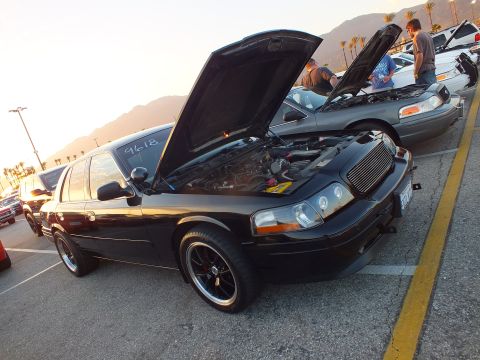 2003 Ford Crown Victoria - Front three-quarter view of a black full-size sedan with its hood raised at a parking-lot car meet.