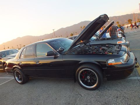 2003 Ford Crown Victoria - lowered black full-size sedan with its hood open, palm trees and mountains in the evening background.