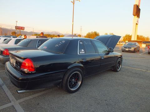 2003 Ford Crown Victoria - Rear three-quarter view of a black full-size sedan with trunk and hood open at a car show.