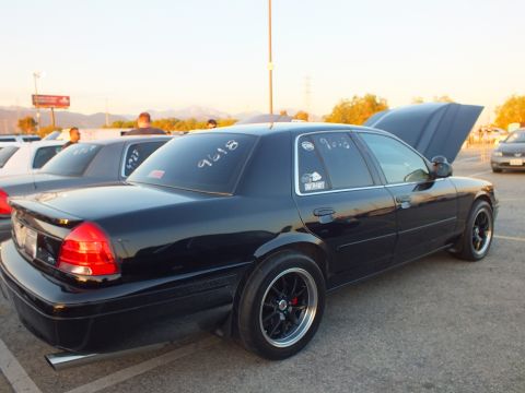 2003 Ford Crown Victoria - Rear view of a black full-size sedan with red taillights and black wheels at a dusk car meet.
