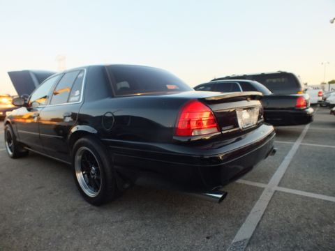 2003 Ford Crown Victoria - Rear three-quarter view of a black full-size sedan with glowing red taillights at dusk.