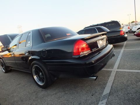 2003 Ford Crown Victoria - Rear view of a black full-size sedan with chrome exhaust tips and black wheels at a car meet.
