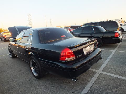 2003 Ford Crown Victoria - Rear view of a black full-size sedan with power lines and a black SUV in the dusk background.