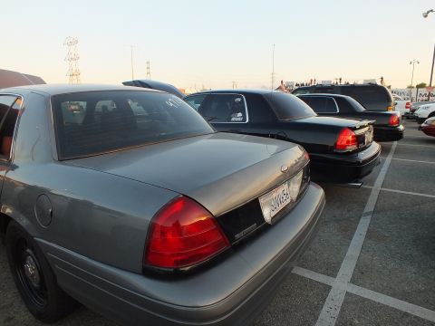 2003 Ford Crown Victoria - Rear of a gray full-size sedan with a California license plate parked beside black sedans at dusk.
