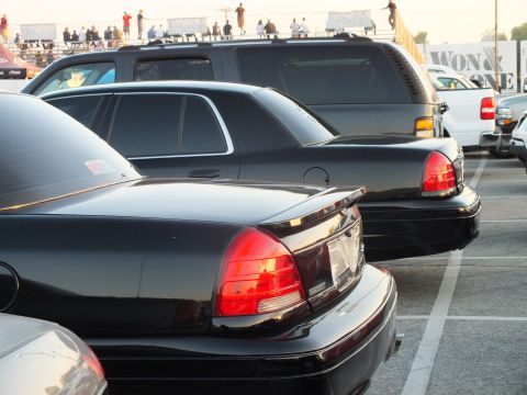 2003 Ford Crown Victoria - row of black full-size sedans and an SUV viewed from the rear at a sunset car meet.