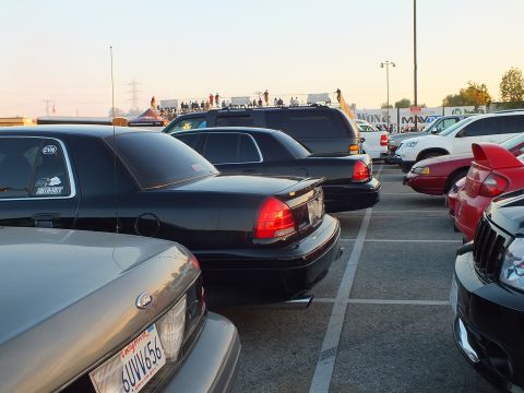 2003 Ford Crown Victoria - lineup of full-size sedans and an SUV in a parking lot with spectators gathered in the distance.