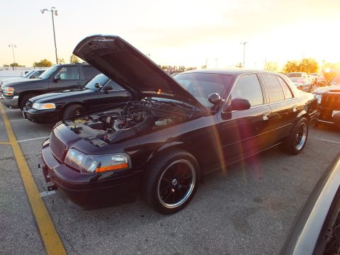 2003 Ford Crown Victoria - Front three-quarter view of a black full-size sedan with open hood and black wheels at sunset.