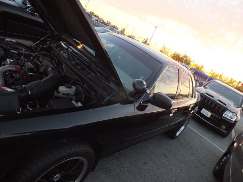 2003 Ford Crown Victoria - black full-size sedan sits with its hood raised at dusk, exposing the engine bay, with an SUV and golden sky in the background.