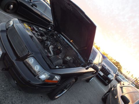 2003 Ford Crown Victoria - black sedan with a billet grille and halo projector headlights sits with its hood open in a lot at sunset, shot at a tilt.