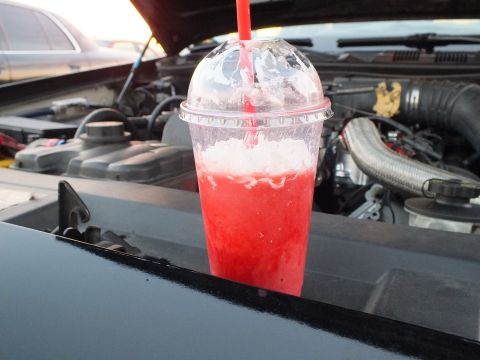 2003 Ford Crown Victoria - red slushie in a clear domed cup is balanced on a black car's cowl panel in front of an open hood and engine bay.