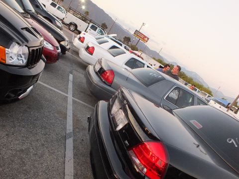 2003 Ford Crown Victoria - diagonal row of vehicles fills a lot at dusk, including a black Jeep, white and black full-size sedans, with hills behind.