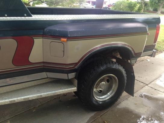 Rear side of a tan and blue Ford F-Series truck with red stripe graphics. Dual rear wheels visible