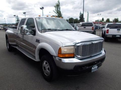 2001 Ford F-350 - A white 2001 Ford F-350 Super Duty dually truck is parked in a lot with other vehicles under a cloudy sky.