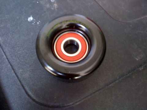 1994 Ford Bronco - Close-up of a pulley wheel with a visible bearing, set against a dark, textured background.