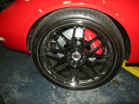 1976 Chevrolet Corvette - Close-up of a red car's wheel assembly, showing custom black rims and performance brakes.