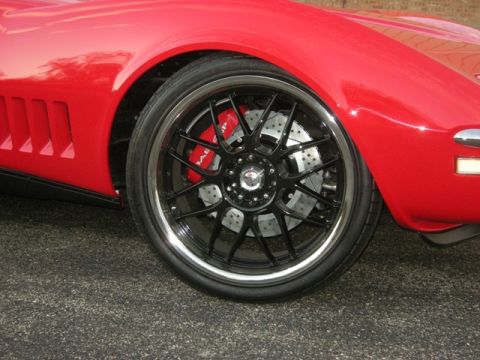 1976 Chevrolet Corvette - Close-up of a red sports car's front wheel custom black rims and high-performance brakes.