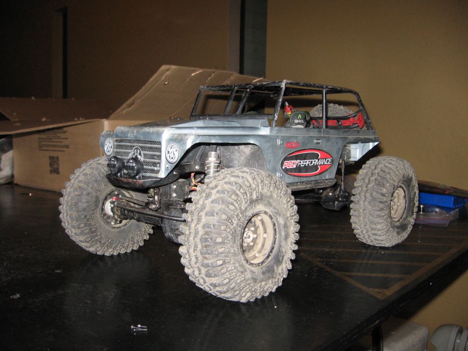 Silver remote control rock crawler with large tires and a roll cage, parked on a dark surface