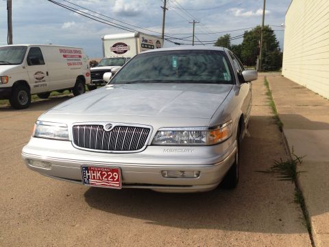 1995 Mercury Grand Marquis - A silver 1995 Mercury Grand Marquis is parked on a paved surface next to a building, with other vehicles in the background.