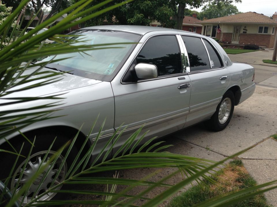 Silver 1995 Mercury Grand Marquis sedan parked on a driveway, partially obscured by palm fronds