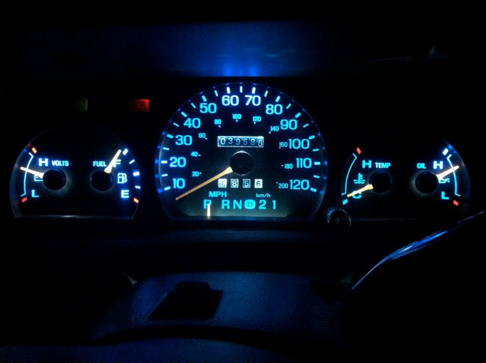 Car dashboard with glowing blue gauges, showing fuel, volts, speed, temp, and oil levels. Odometer reads 039596