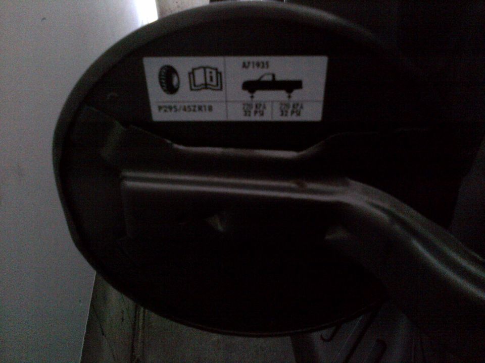 Black circular part with a sticker showing tire size P295/45ZR18 and inflation pressures