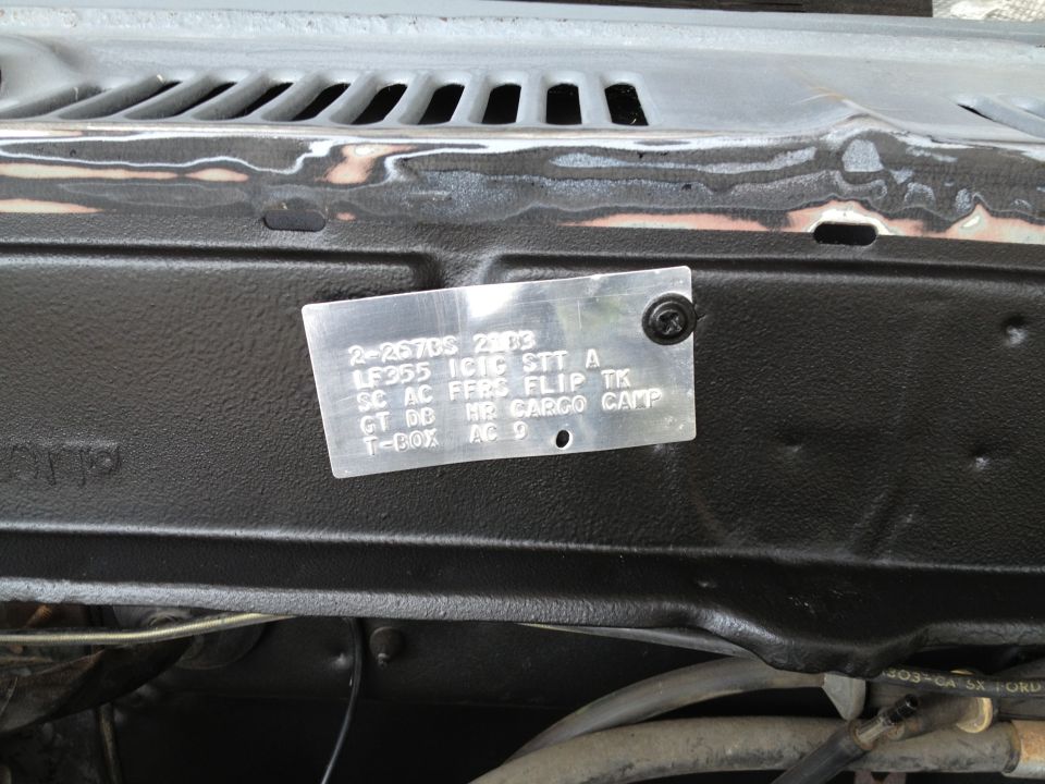 Close-up of a VIN plate with text including 'LF355 ICIC STT A' and 'CARGO CAM', attached to a black painted surface in an engine bay