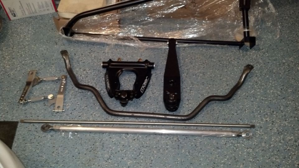 Various black and silver automotive suspension components laid out on a speckled floor. Includes sway bars and adjustable linkages