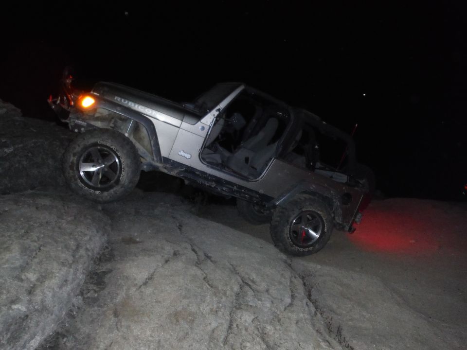 Silver 2005 Jeep Wrangler Rubicon climbing rocks at night, doors off
