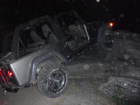 2005 Jeep Wrangler - A black Jeep Wrangler navigates rocky terrain in the dark, its silver rear fenders catching the light.