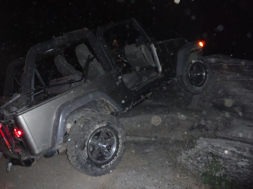 Black Jeep Wrangler with silver rear fenders, off-roading at night on rocks