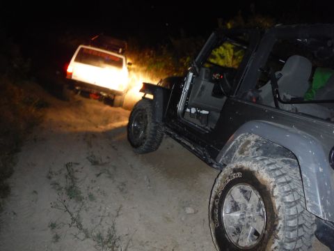 2005 Jeep Wrangler - Two off-road vehicles navigate a dirt path at night, illuminated by headlights.