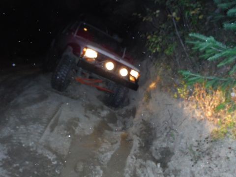 2005 Jeep Wrangler - A Jeep CJ-7 navigates a challenging dirt trail in the dark, its headlights illuminating the path ahead.