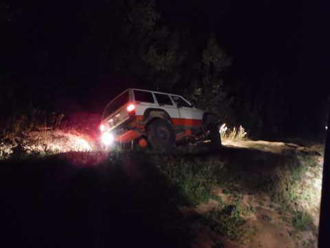 2005 Jeep Wrangler - A Jeep Cherokee XJ navigates a dark, wooded trail at night, its headlights illuminating the path ahead.