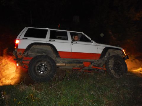 2005 Jeep Wrangler - A modified Jeep Cherokee XJ navigates rough terrain at night, its headlights illuminating the path ahead.