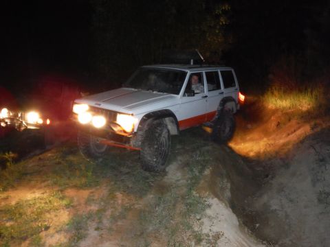 2005 Jeep Wrangler - A white Jeep Cherokee XJ with orange trim and auxiliary lights navigates an off-road trail at night.