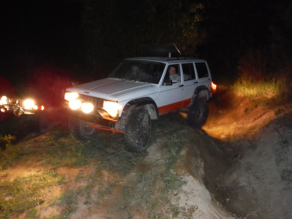 White Jeep Cherokee XJ with orange trim and off-road lights driving at night