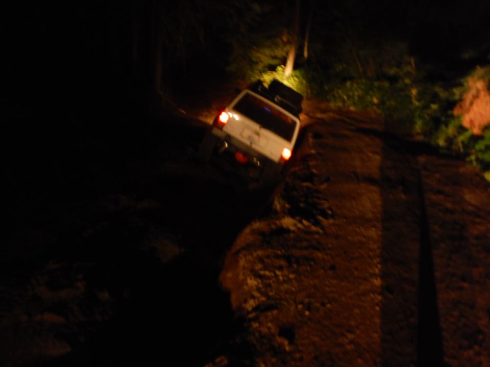 White 2005 Jeep Wrangler parked on a dirt road at night, with taillights illuminated