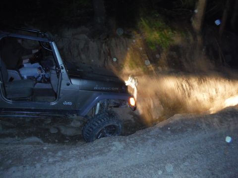 2005 Jeep Wrangler - A Jeep Wrangler navigates a tight off-road trail in the dark, illuminated by its headlights.