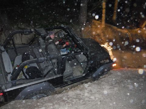 2005 Jeep Wrangler - A black 2005 Jeep Wrangler navigates a muddy trail at night, with its tires deep in the dirt.