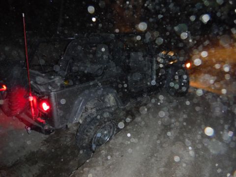2005 Jeep Wrangler - A dark Jeep Wrangler is seen from the rear at night, with its brake lights illuminated.